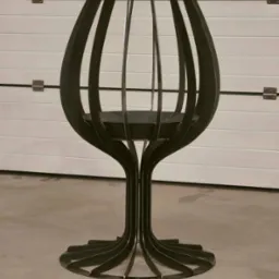 Metalowa konstrukcja przypominająca kielich, wykonana ze spawanych elementów, na tle białej bramy garażowej. Nowoczesny, minimalistyczny design.