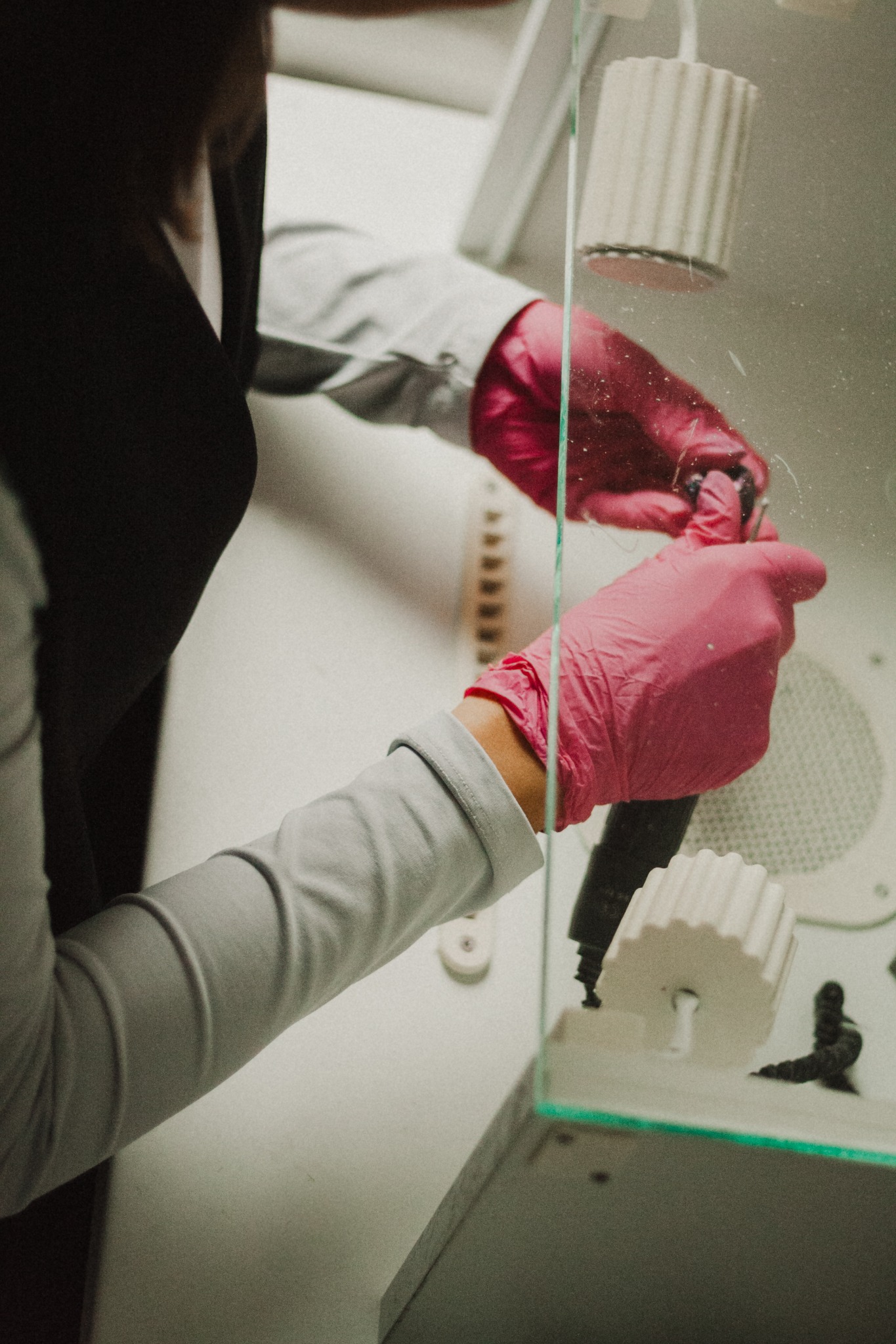 Praca w laboratorium: Ręce w różowych rękawicach manipulują narzędziem w sterylnym boksie, obok widoczne białe elementy i spiralny notatnik.