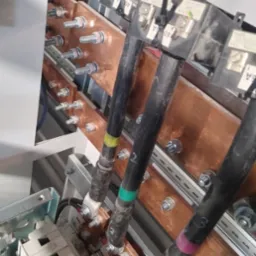 Szyny zbiorcze z podłączonymi przewodami w rozdzielnicy, widok z góry, instalacja elektryczna w Legionowie. Miedziane elementy i czarne kable.