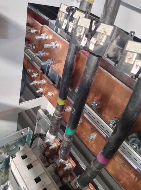 Szyny zbiorcze z podłączonymi przewodami w rozdzielnicy, widok z góry, instalacja elektryczna w Legionowie. Miedziane elementy i czarne kable.