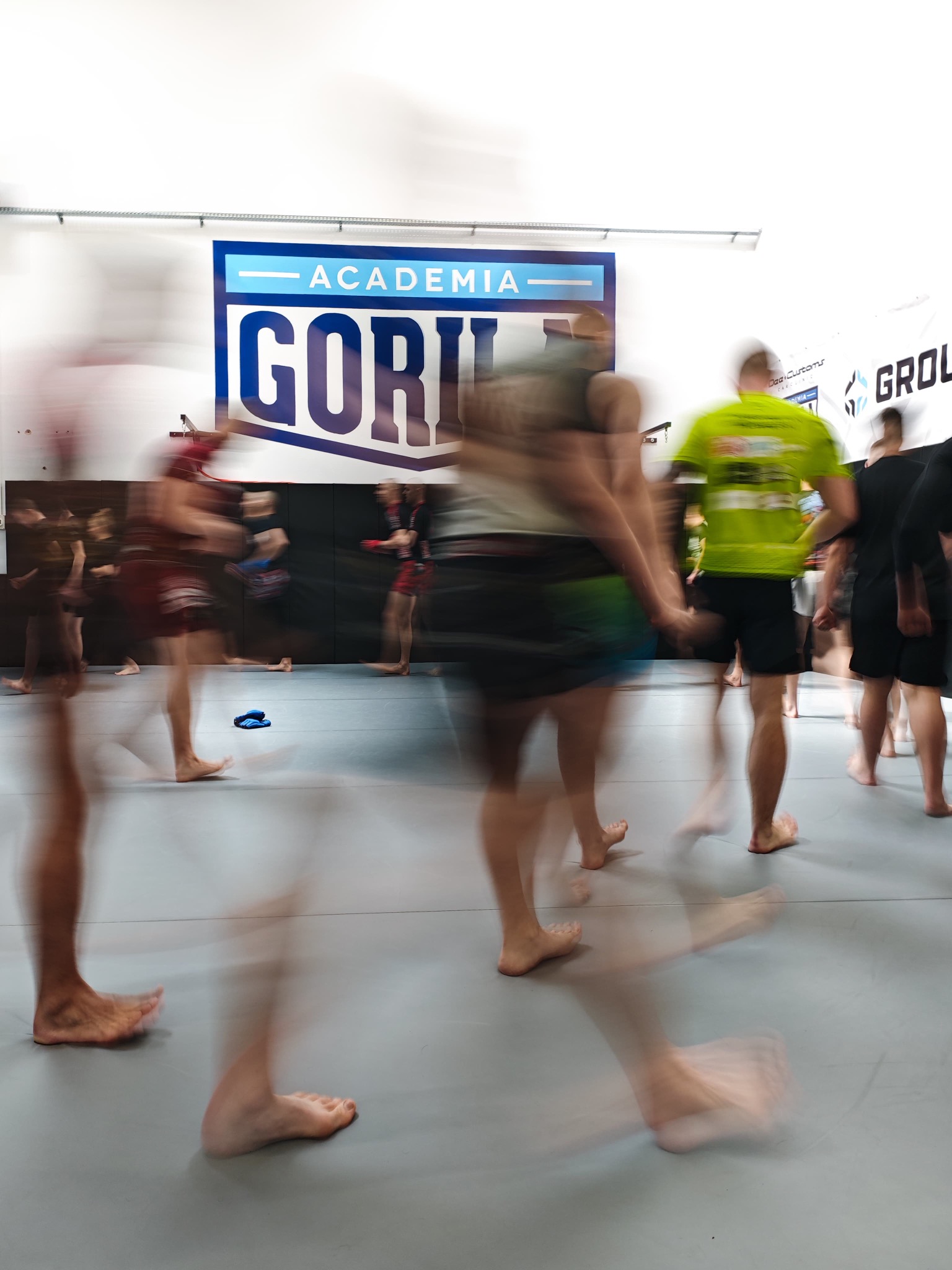 Dynamiczne ujęcie grupy osób podczas treningu w Akademii Gorila, w ruchu, z widocznymi elementami wyposażenia sali treningowej.