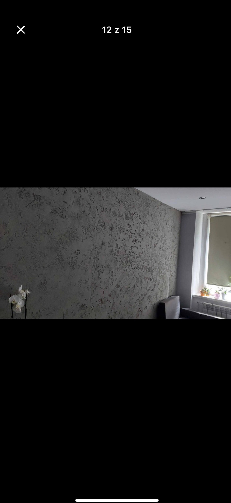 Szara ściana z dekoracyjną strukturą w pokoju, obok okno z roślinami i biały storczyk. Teksturowana powierzchnia ściany.