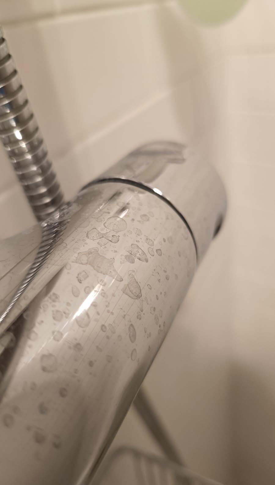 Bateria umywalkowa ze śladami osadu z kamienia i mydła, widoczne zacieki. Chromowana powierzchnia z bliska, słabe oświetlenie.