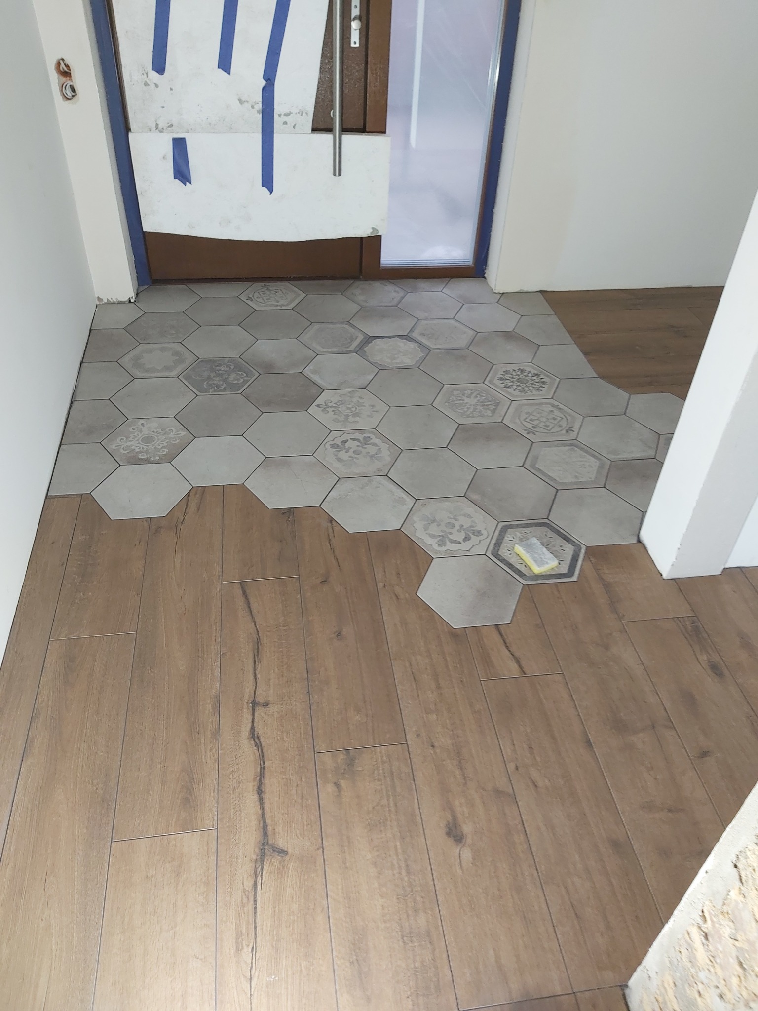 Układanie heksagonalnych płytek podłogowych z wzorem, częściowo zakończone, w połączeniu z panelami imitującymi drewno. Widoczna gąbka do fugowania.