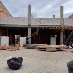 ARBUD Artur Michalak - Budowa domu z betonu komórkowego w stanie surowym otwartym, widoczne ściany, słupy, strop, drewniane elementy szalunku i pracownik z narzędziem.