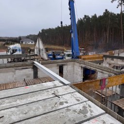 ARBUD Artur Michalak - Budowa domu z pustaków: widok z góry na strop z płyt prefabrykowanych, dźwigiem transportowane są kolejne elementy. W tle las i fragment budynku.