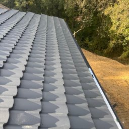 ARBUD Artur Michalak - Szary dach z blachy trapezowej, widok z góry, z poziomnicą w rogu, na tle drzew. Widoczne mocowania blachy. Krycie dachu w trakcie realizacji.