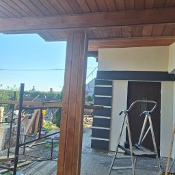 ARBUD Artur Michalak - Drewniana konstrukcja werandy w Kłecku, widok w trakcie budowy. Słup nośny, podbitka dachowa z desek, rusztowanie i drabina. Elementy wykończenia elewacji budynku.