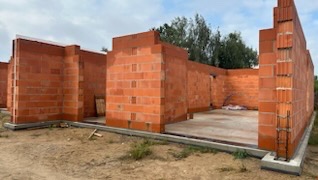 Wznoszone ściany z czerwonej cegły ceramicznej na fundamencie, widok z zewnątrz, na placu budowy w pochmurny dzień. Częściowo ukończone ściany domu.