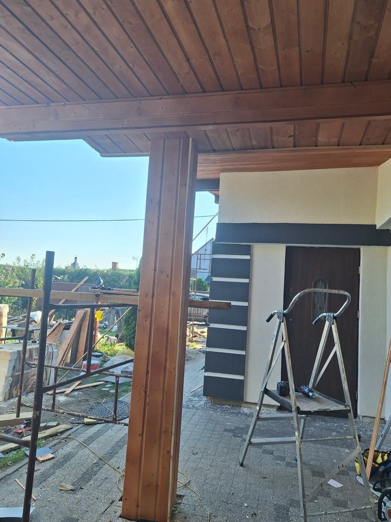 Drewniana konstrukcja werandy w Kłecku, widok w trakcie budowy. Słup nośny, podbitka dachowa z desek, rusztowanie i drabina. Elementy wykończenia elewacji budynku.