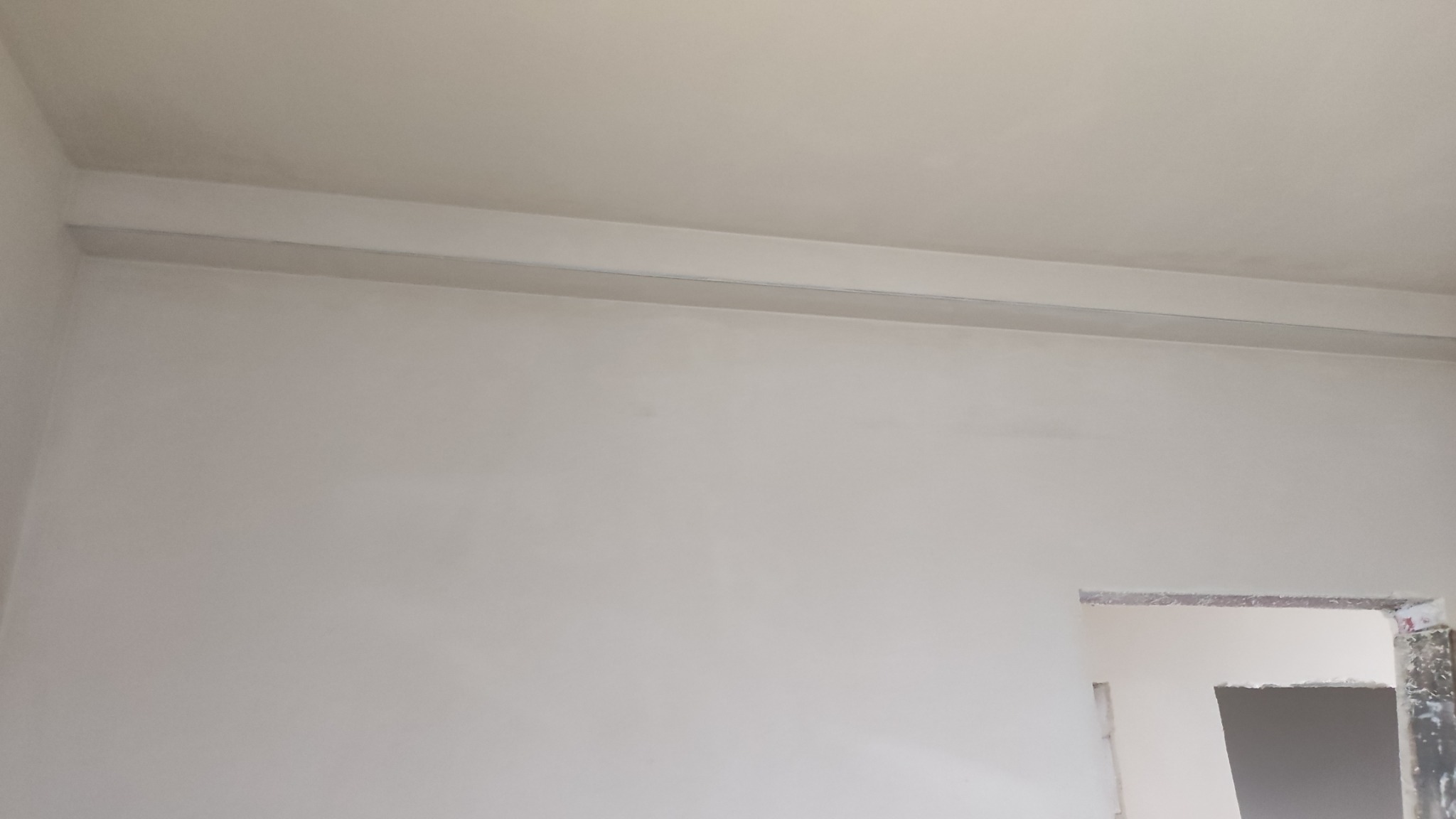 Gładka, jasna ściana po szpachlowaniu w Grzybowie, widoczny fragment sufitu i ościeżnica drzwi. Minimalistyczne wykończenie wnętrza.