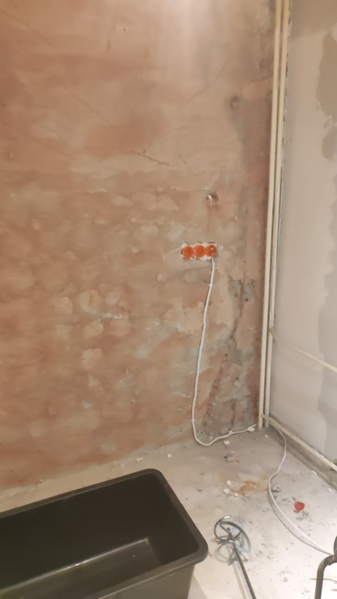 Przygotowana ściana pod gładź z puszkami elektrycznymi, widoczna instalacja, pojemnik i mieszadło do gładzi. Surowy stan przed wykończeniem.