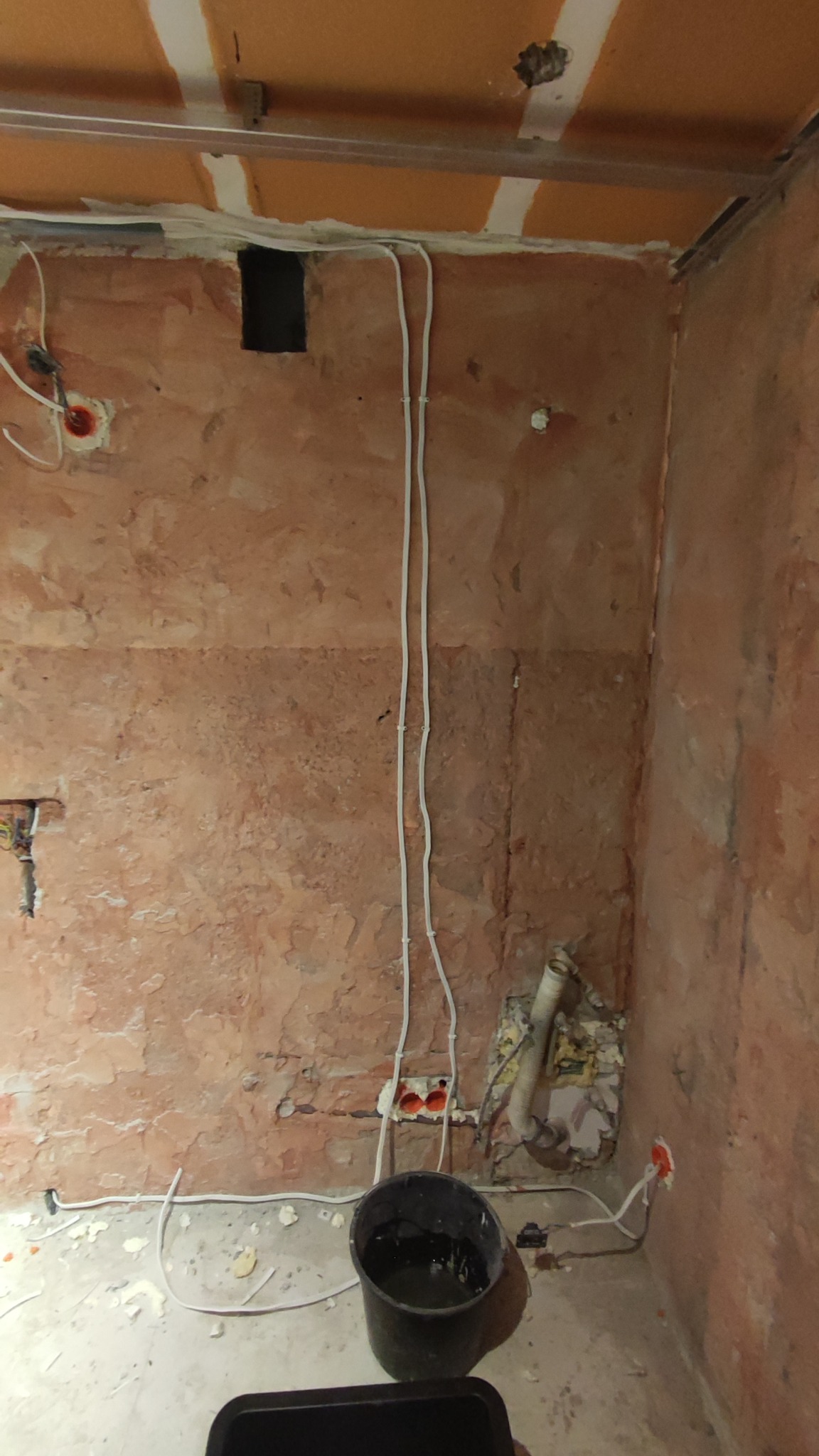 Pokój w trakcie remontu: ściany z surowym tynkiem, instalacja elektryczna na wierzchu, widoczne puszki elektryczne, fragment stelażu sufitu podwieszanego.