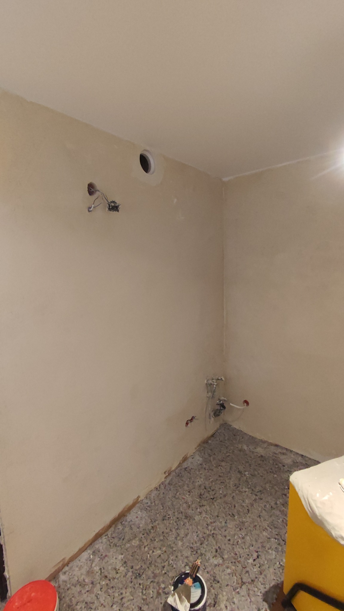 Pokój po gładziowaniu, z zabezpieczoną podłogą i widocznymi puszkami elektrycznymi. Ściany przygotowane do malowania, widoczne niedoskonałości wykończenia.