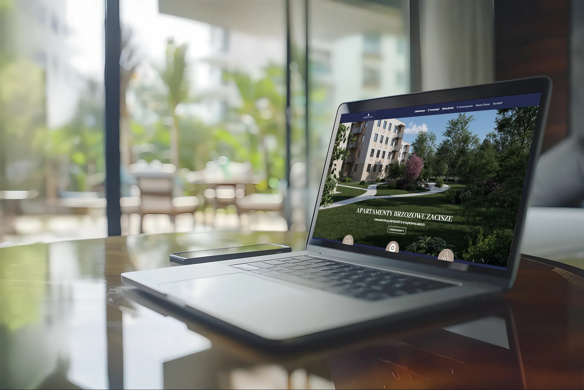Laptop prezentuje stronę internetową z wizualizacją osiedla 'Apartamenty Brzozowe Zacisze' na tle słonecznego balkonu. Obok leży smartfon.