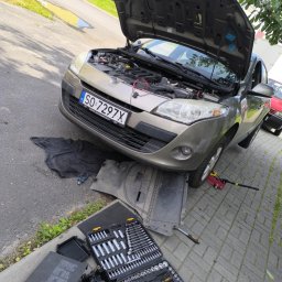 Vitucky - Beżowy samochód z otwartą maską na chodniku. Widoczny zestaw narzędzi, podnośnik i czarna mata. Tablica rejestracyjna SO 7297X. Prace naprawcze na zewnątrz.