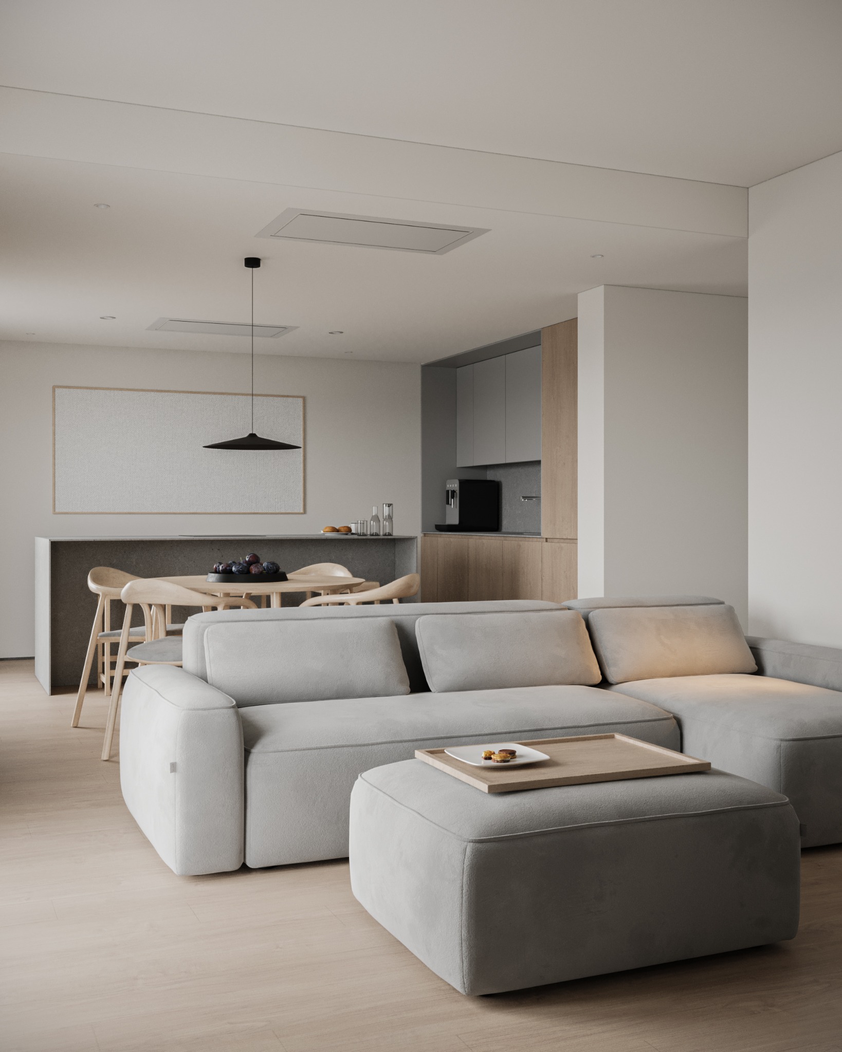 Neutralna tonacja salonu z szarą sofą modułową i drewnianym stolikiem kawowym. W tle jadalnia z owocami na stole i minimalistyczna kuchnia w drewnie i szarości.