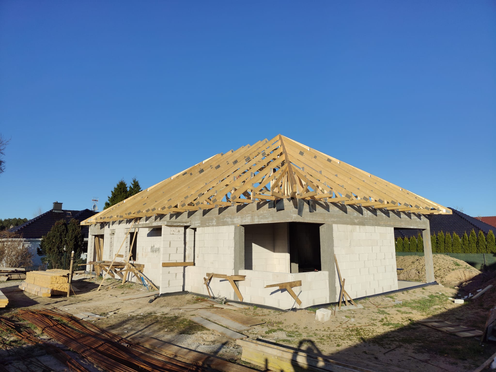Budowa domu jednorodzinnego w trakcie realizacji. Widoczna konstrukcja więźby dachowej na ścianach z betonu komórkowego w słoneczny dzień.