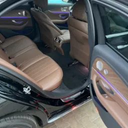 Luksusowe wnętrze czarnego samochodu z brązową skórzaną tapicerką, podświetleniem LED i otwartymi drzwiami, ukazujące dbałość o detale i komfort podróży.