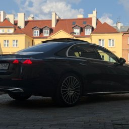 MAT VIP TRANSPORT - Elegancki, czarny samochód osobowy marki Mercedes, zaparkowany na brukowanej ulicy, z budynkami w tle. Widoczny fragment tablicy rejestracyjnej.