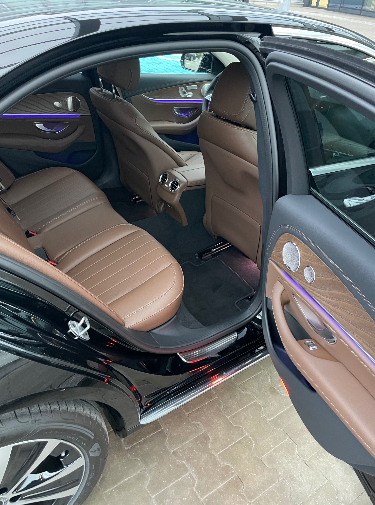 Luksusowe wnętrze czarnego samochodu z brązową skórzaną tapicerką, podświetleniem LED i otwartymi drzwiami, ukazujące dbałość o detale i komfort podróży.