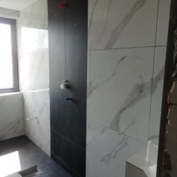 Andrzej Ludwig - Nowoczesna łazienka z czarną ścianą prysznicową i marmurowymi płytkami. Widoczne baterie i odpływ liniowy. Minimalistyczny design z dbałością o detale.