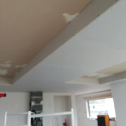 Andrzej Ludwig - Sufit podwieszany w trakcie prac wykończeniowych, widoczne łączenia płyt gipsowych przed szpachlowaniem. W tle rusztowanie i nagrzewnica.