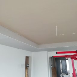 Andrzej Ludwig - Wnętrze w trakcie szpachlowania sufitu, widoczna lampa na statywie i podnośnik do płyt gipsowo-kartonowych. Ściany pomalowane na biało, sufit w kolorze beżowym.