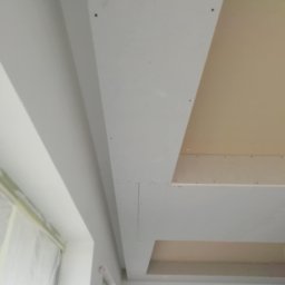 Andrzej Ludwig - Sufit podwieszany z płyt gipsowo-kartonowych, częściowo wykończony, widoczne łączenia płyt i przygotowane do szpachlowania, okno zabezpieczone folią malarską.