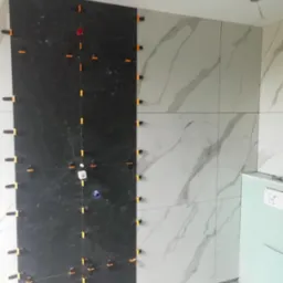 Układanie płytek: czarne i białe marmurowe płytki na ścianie, z pomarańczowymi klipsami poziomującymi, widoczne fragmenty podłogi i narzędzi glazurniczych.