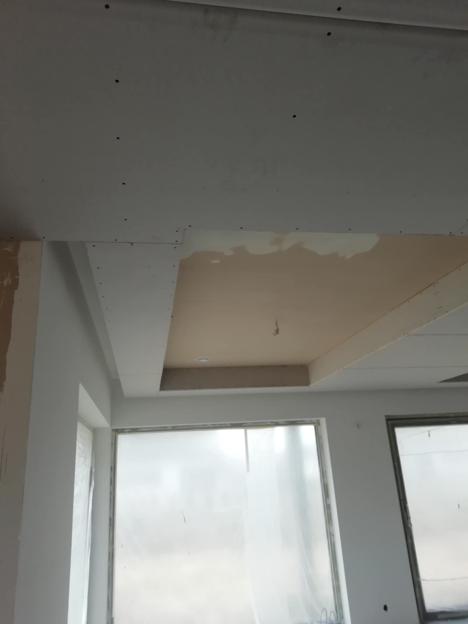 Sufit podwieszany z płyt kartonowo-gipsowych w trakcie szpachlowania. Okna zabezpieczone folią malarską. Widoczne ślady po wkrętach.