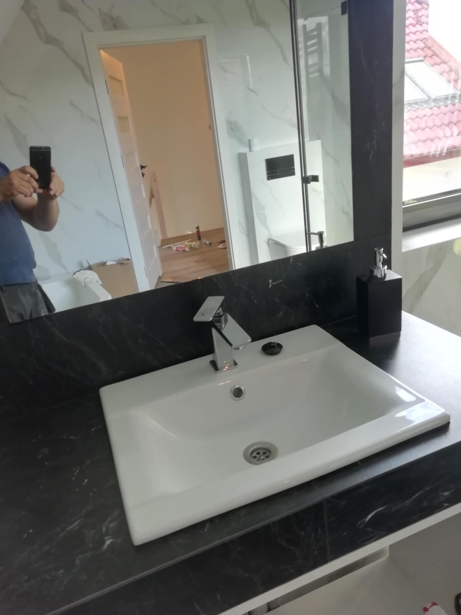 Biała umywalka nablatowa na czarnym blacie w wyremontowanej łazience w Słupsku. W lustrze odbicie części pomieszczenia i osoby robiącej zdjęcie.