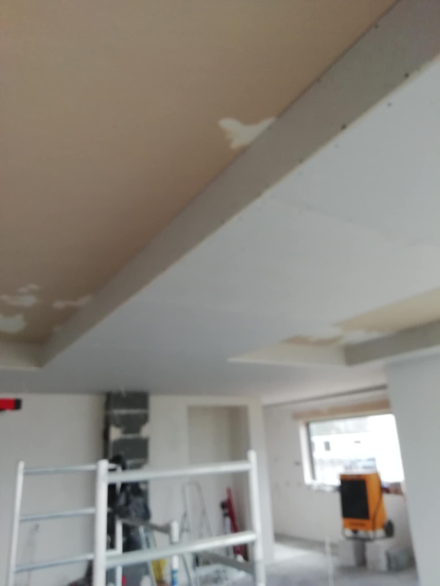 Sufit podwieszany w trakcie prac wykończeniowych, widoczne łączenia płyt gipsowych przed szpachlowaniem. W tle rusztowanie i nagrzewnica.