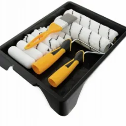 Zestaw malarski w czarnej kuwecie: wałki z czarnymi paskami, małe białe wałki, pędzel z żółtą rączką i dwie rączki do wałków z żółtymi uchwytami.