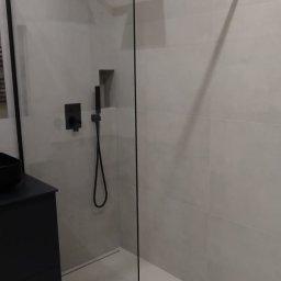 Nikodem Pawłowski - Nowoczesna kabina prysznicowa walk-in z czarnymi elementami, minimalistyczny design, oświetlenie LED w łazience z jasnymi płytkami.