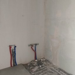 Nikodem Pawłowski - Surowy stan łazienki w trakcie remontu: widoczne rury instalacji wodnej i ślady po kuciu w posadzce, przygotowanie do dalszych prac wykończeniowych.