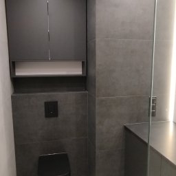 Nikodem Pawłowski - Nowoczesna łazienka w odcieniach szarości z czarną armaturą i szafkami, minimalistyczny design, realizacja w Rzeszowie. Uwagę zwraca szklana kabina.