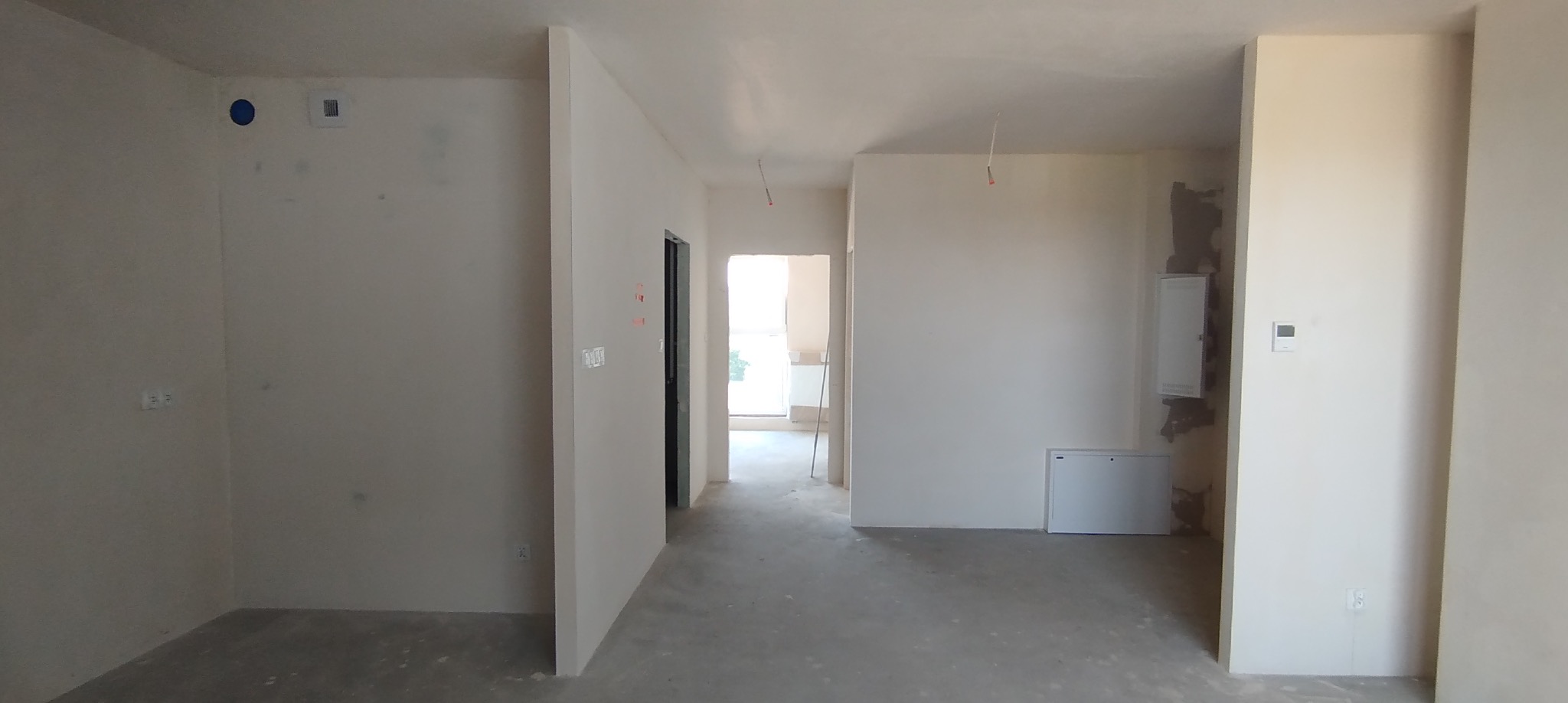 Wnętrze w trakcie remontu: świeżo wyszpachlowane ściany, surowy beton na podłodze, widoczne instalacje. Przygotowanie do malowania w jasnym, przestronnym pomieszczeniu.