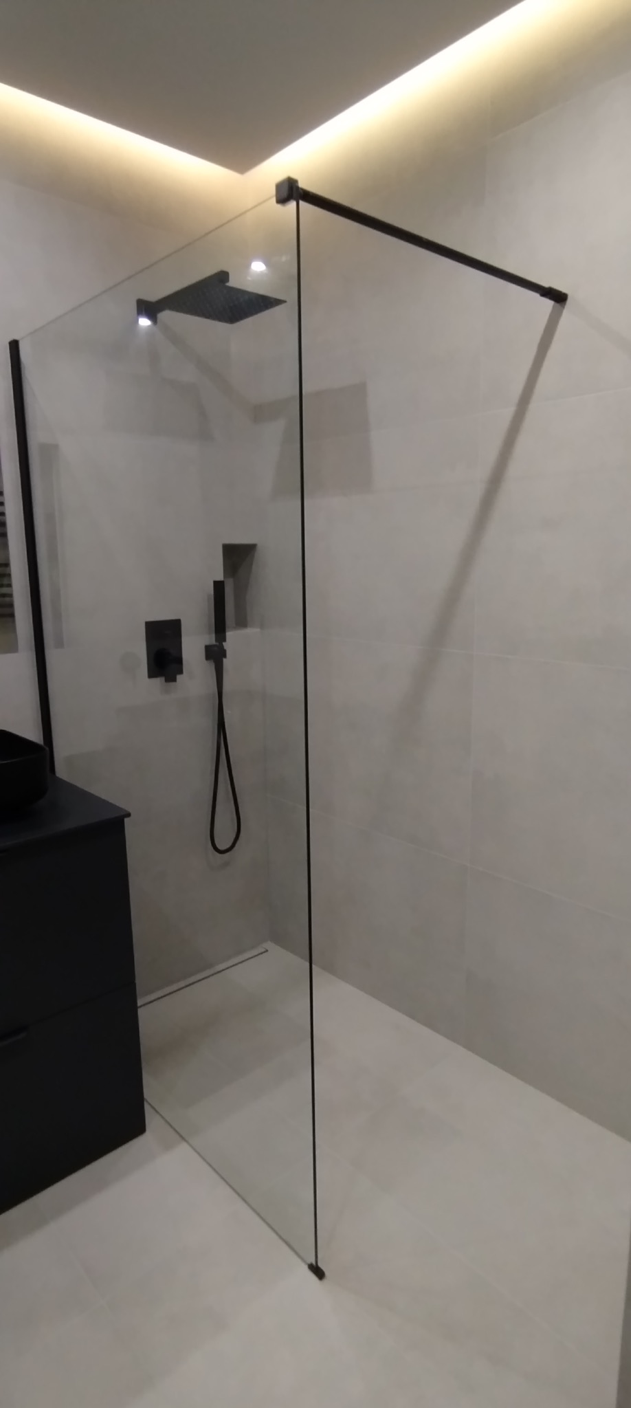 Nowoczesna kabina prysznicowa walk-in z czarnymi elementami, minimalistyczny design, oświetlenie LED w łazience z jasnymi płytkami.