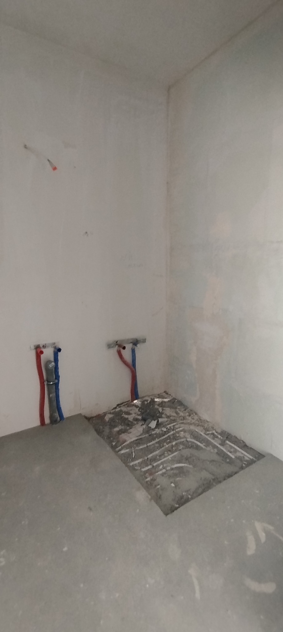 Surowy stan łazienki w trakcie remontu: widoczne rury instalacji wodnej i ślady po kuciu w posadzce, przygotowanie do dalszych prac wykończeniowych.