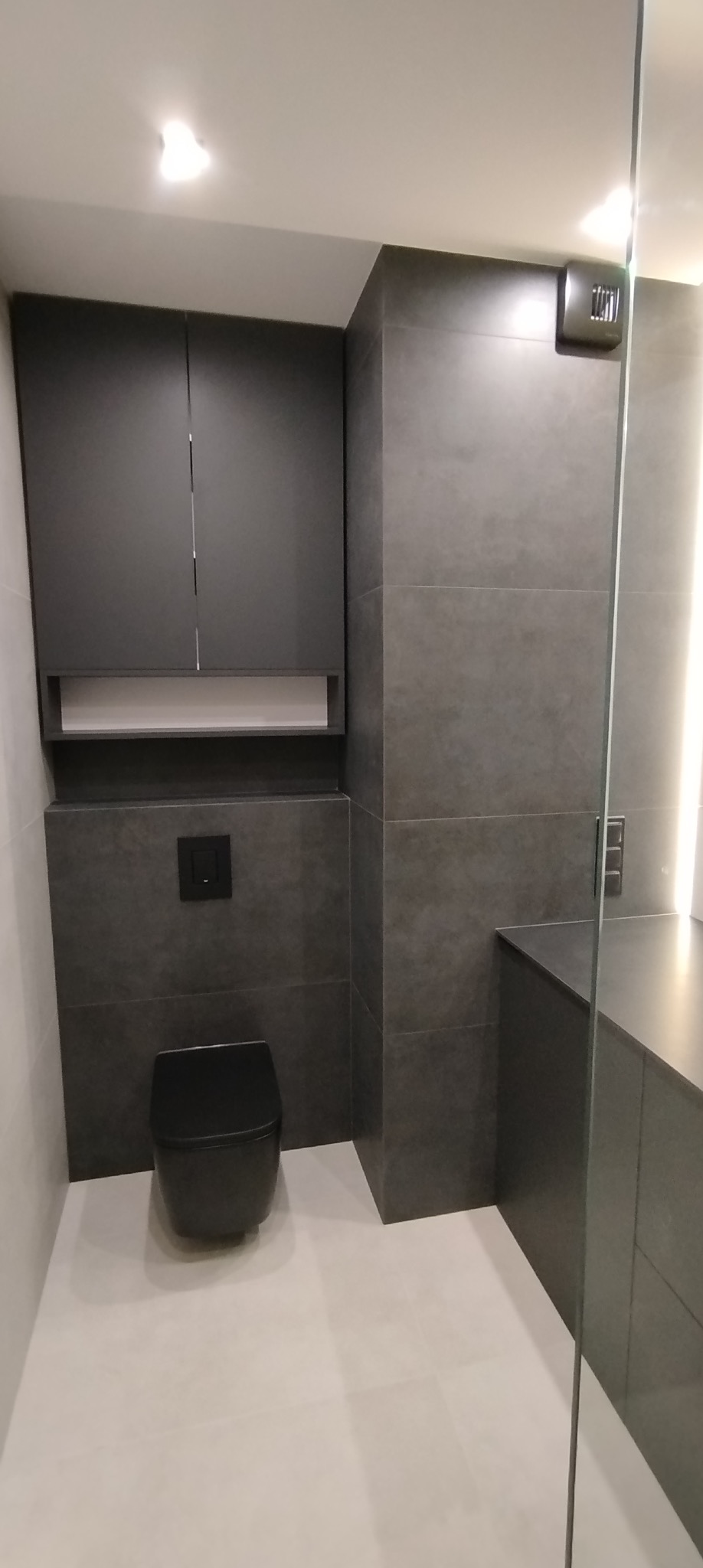 Nowoczesna łazienka w odcieniach szarości z czarną armaturą i szafkami, minimalistyczny design, realizacja w Rzeszowie. Uwagę zwraca szklana kabina.