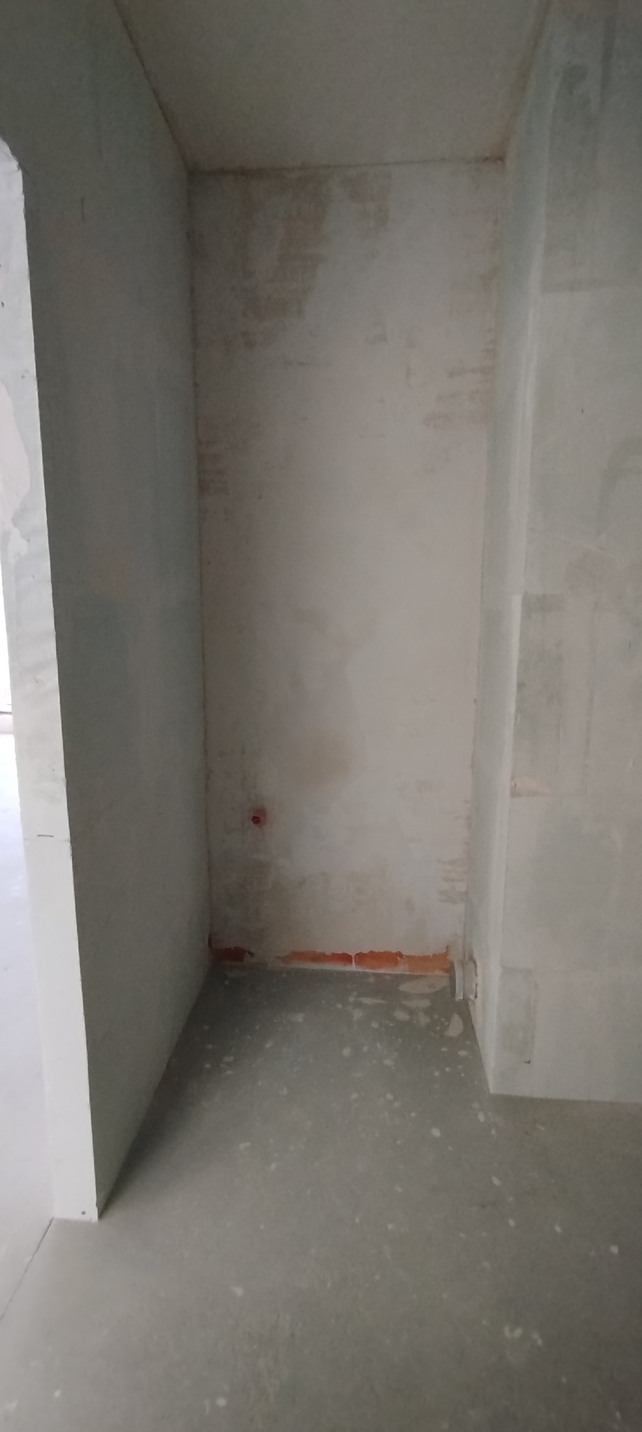 Surowe wnętrze w trakcie remontu: ściany przygotowane do szpachlowania, widoczne ślady po instalacjach, surowy beton na podłodze. Czerwone cegły przy podłodze.