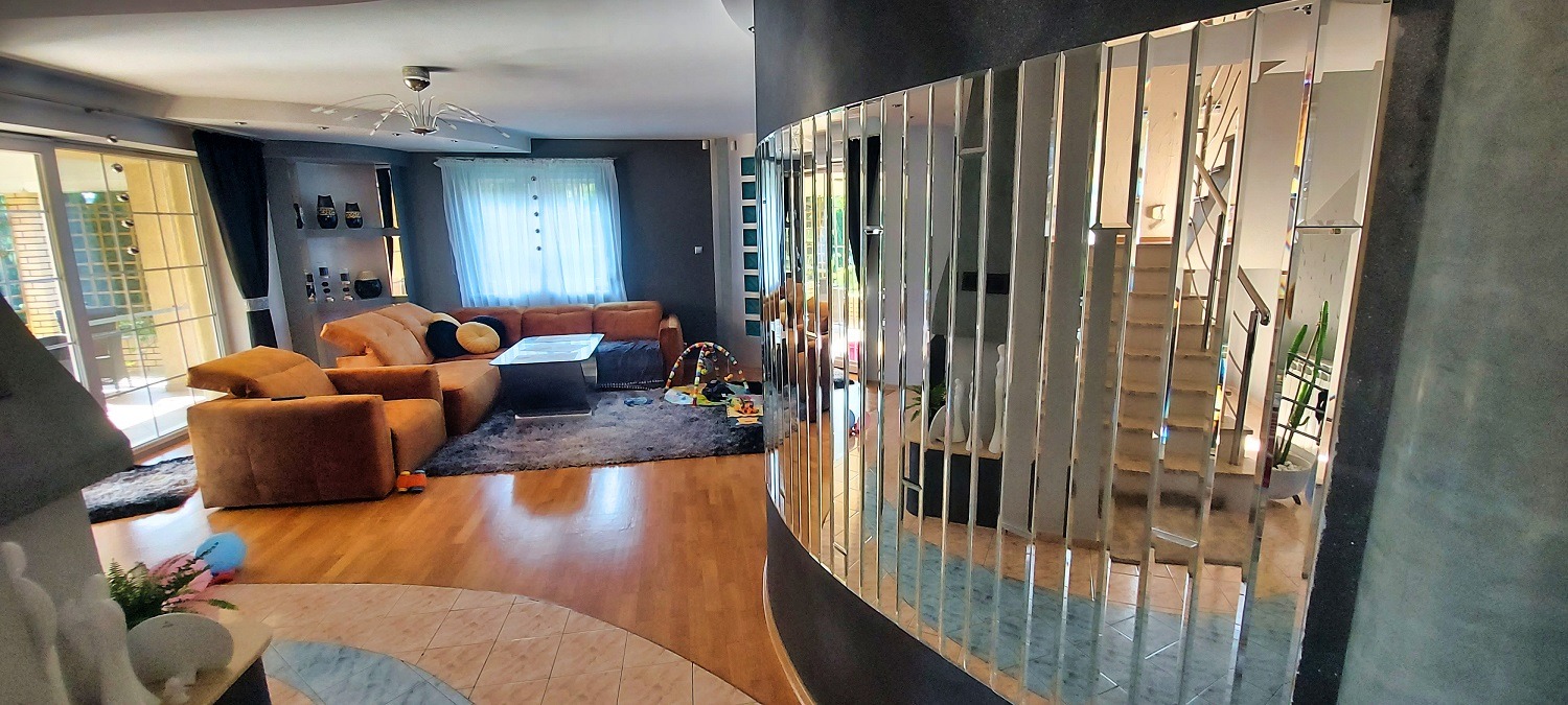 Salon z narożnikiem, dywanem i ścianą z pionowych luster, odbijających schody. Lustra tworzą unikalny element dekoracyjny wnętrza.