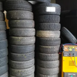 Stosy opon zimowych i letnich z żółtym urządzeniem do obsługi klimatyzacji samochodowej North Cape na pierwszym planie.