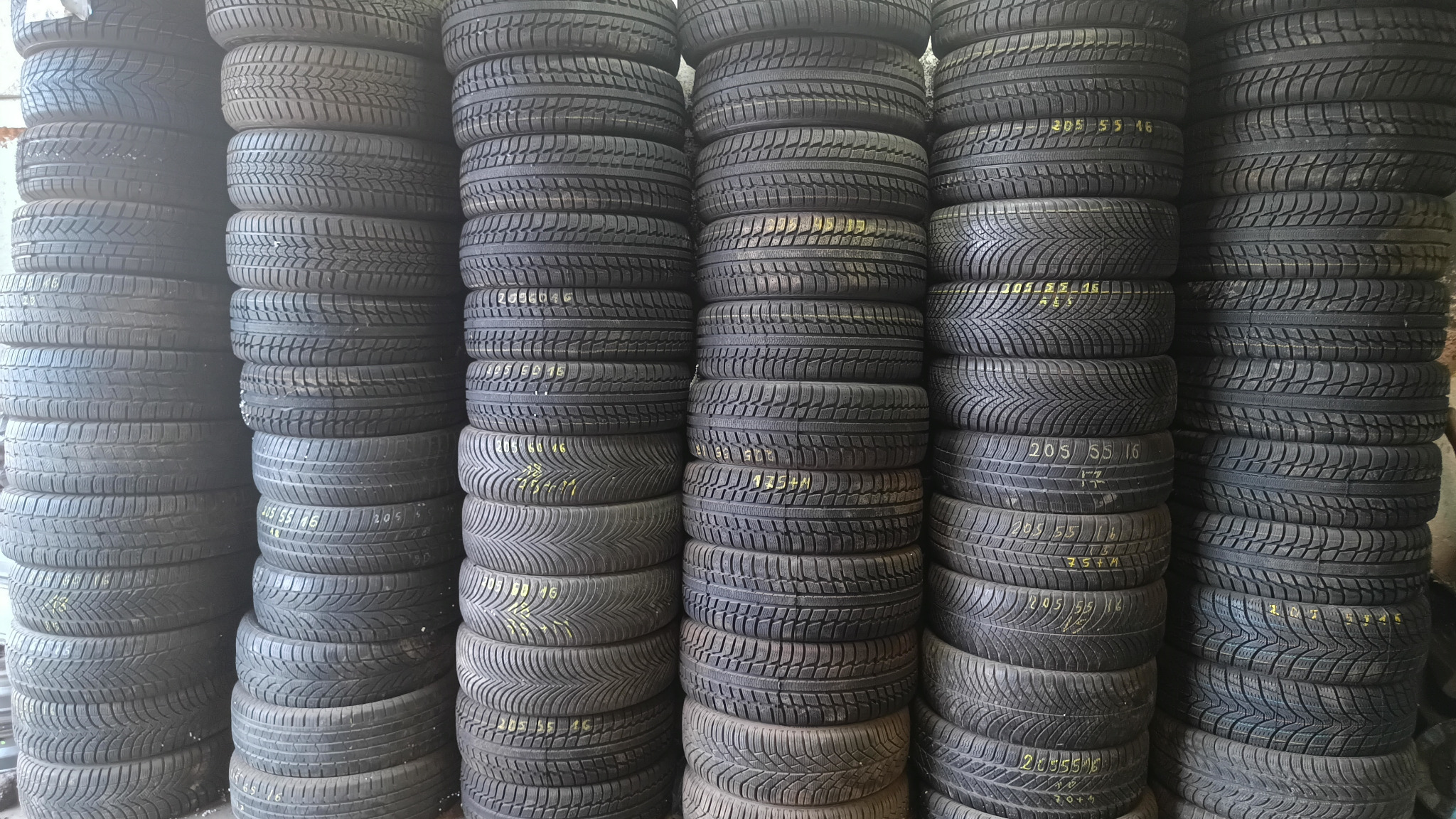 Stosy opon samochodowych ułożone pionowo, widoczne różne bieżniki i rozmiary, niektóre z żółtymi oznaczeniami.