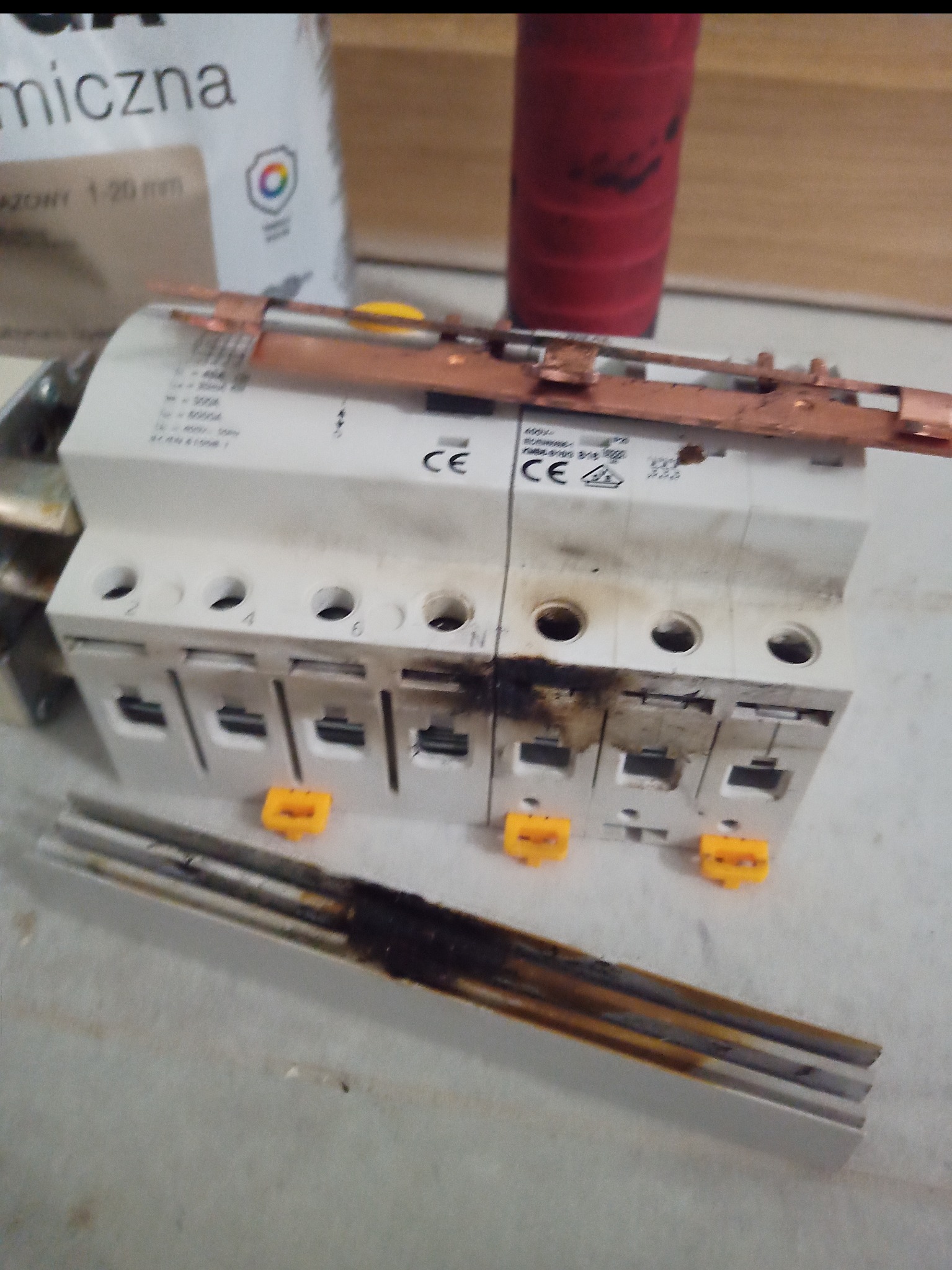 Uszkodzona, przepalona listwa zasilająca i wyłączniki nadprądowe z widocznymi śladami pożaru. Awaria instalacji elektrycznej.