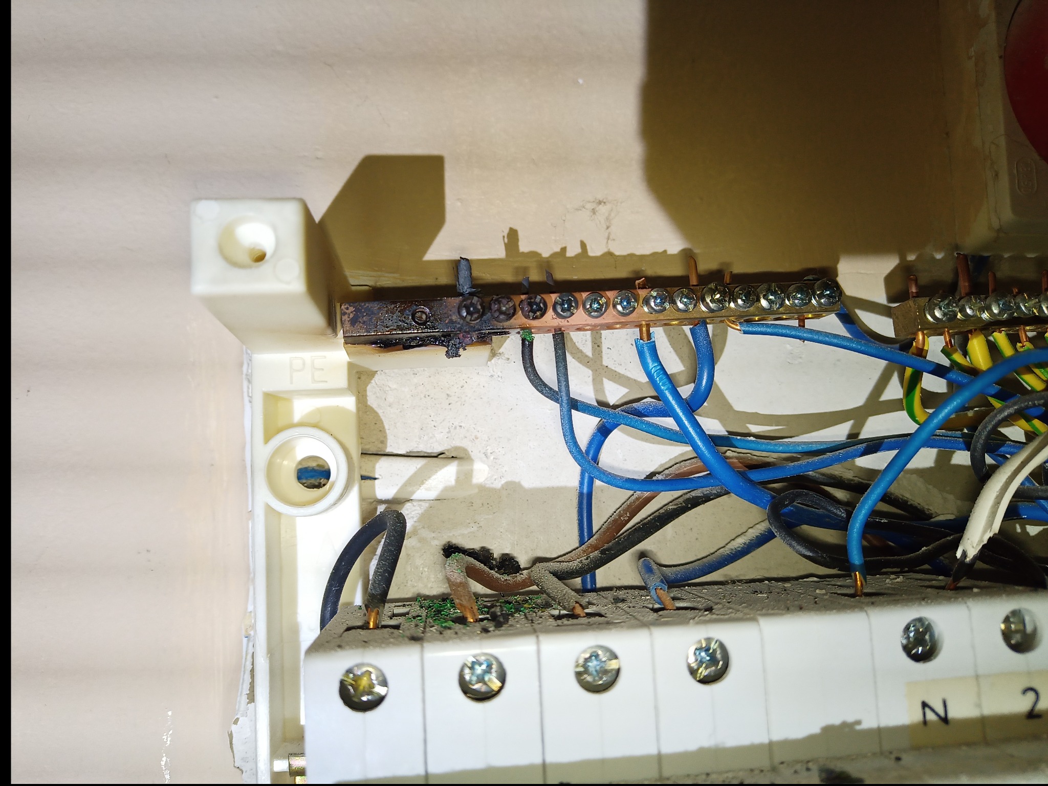 Spalona listwa zaciskowa w skrzynce elektrycznej. Uszkodzone przewody, zwęglona obudowa. Widoczne ślady pożaru i przepięcia. Awaria instalacji elektrycznej.