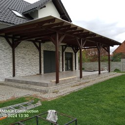 Tynki maszynowe - Zadaszenie tarasu z drewnianą konstrukcją i jasną tkaniną, widok z zewnątrz. Na pierwszym planie trawnik i drabina. Tło to elewacja domu.