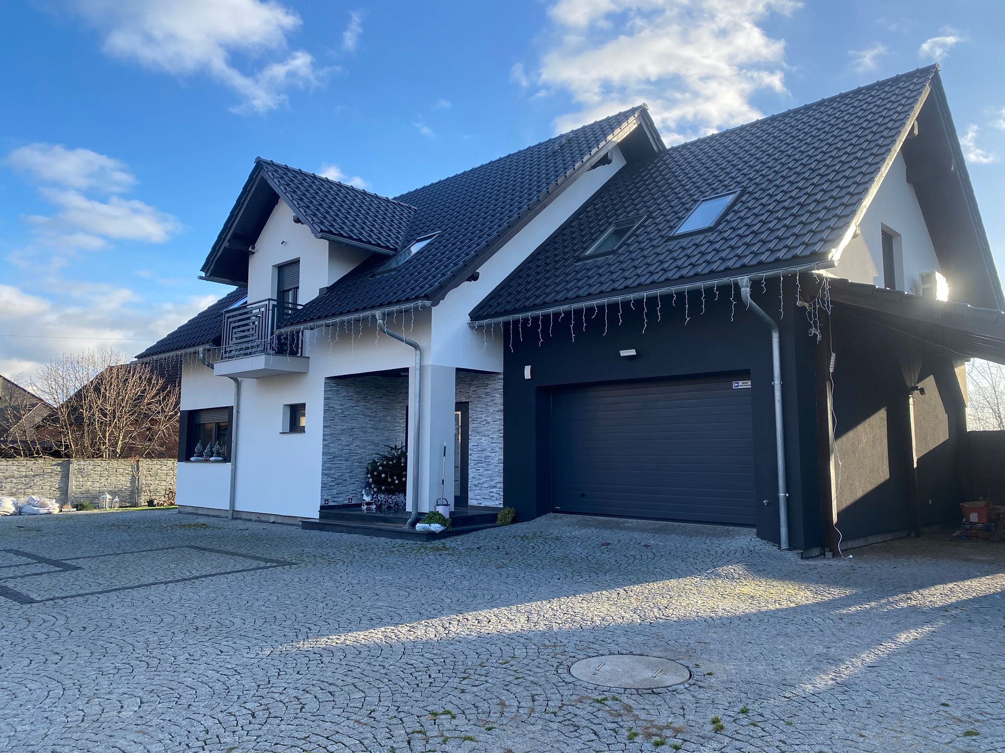 Elegancki dom jednorodzinny w Głogowie z czarno-białą elewacją, garażem i zadbanym podjazdem z kostki. Nowoczesny design z elementami dekoracyjnymi.