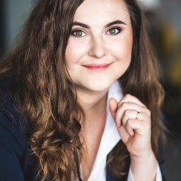 ANCZEWSKA I PUŃKO KANCELARIA ADWOKACKO-RADCOWSKA S.C. - Portret kobiety w ciemnej marynarce i białej koszuli, z delikatnym uśmiechem i pierścionkiem na palcu, na rozmytym tle.